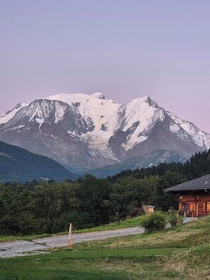 Ein Berg mit schneebedeckten Gipfeln, ein bewaldetes Tal und ein kleines Gebäude mit einem geneigten Dach.