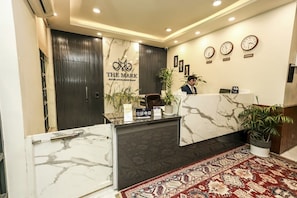 Zona de recepció d'un hotel amb un taulell de marbre, un rellotge i una planta en test.
