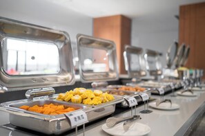 Un buffet proposant une variété de plats, notamment des dés de maïs et d’orange, présentés sur un comptoir avec des ustensiles de service en métal.