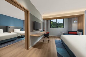 Quarto de hotel moderno com uma cama grande, uma escrivaninha com cadeira, televisão e janela com vista para árvores.