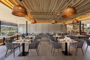 A restaurant with a modern interior, featuring a central dining area with tables and chairs, a ceiling with hanging lights, and a view of the outdoors. - Hotel Maspalomas Villas by Dunas - Adults Only (San Bartolomé de Tirajana)