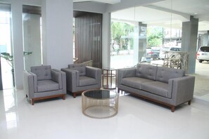 A modern lobby with a grey sofa set, two armchairs, and a round coffee table. - Grand Kutilang Syariah (Bandar Lampung)