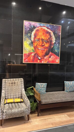 A modern interior with a sofa and armchair, a large framed artwork on the wall, and a potted plant. - Cape Town – A Home Like No Other (Cape Town)