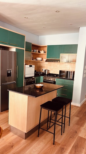 A modern kitchen with green cabinets, stainless steel appliances, and a central island with stools. - Cape Town – A Home Like No Other (Cape Town)