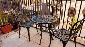 A balcony with a wrought iron table and chairs, potted plants, and a view of the street. - Cape Town – A Home Like No Other (Cape Town)