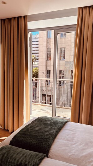 A hotel room with a large window, a bed with pillows, and a view of the street and buildings outside. - Cape Town – A Home Like No Other (Cape Town)
