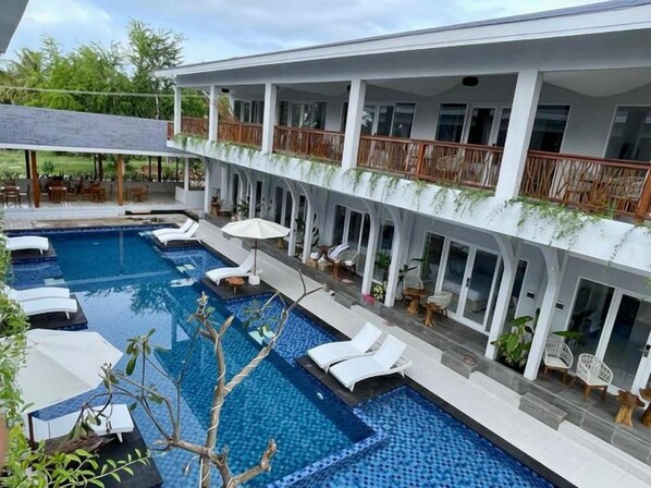 A hotel with a large outdoor swimming pool, lounge chairs, and a covered seating area. - Sea Shell Resort Gili Trawangan (Gili Trawangan)