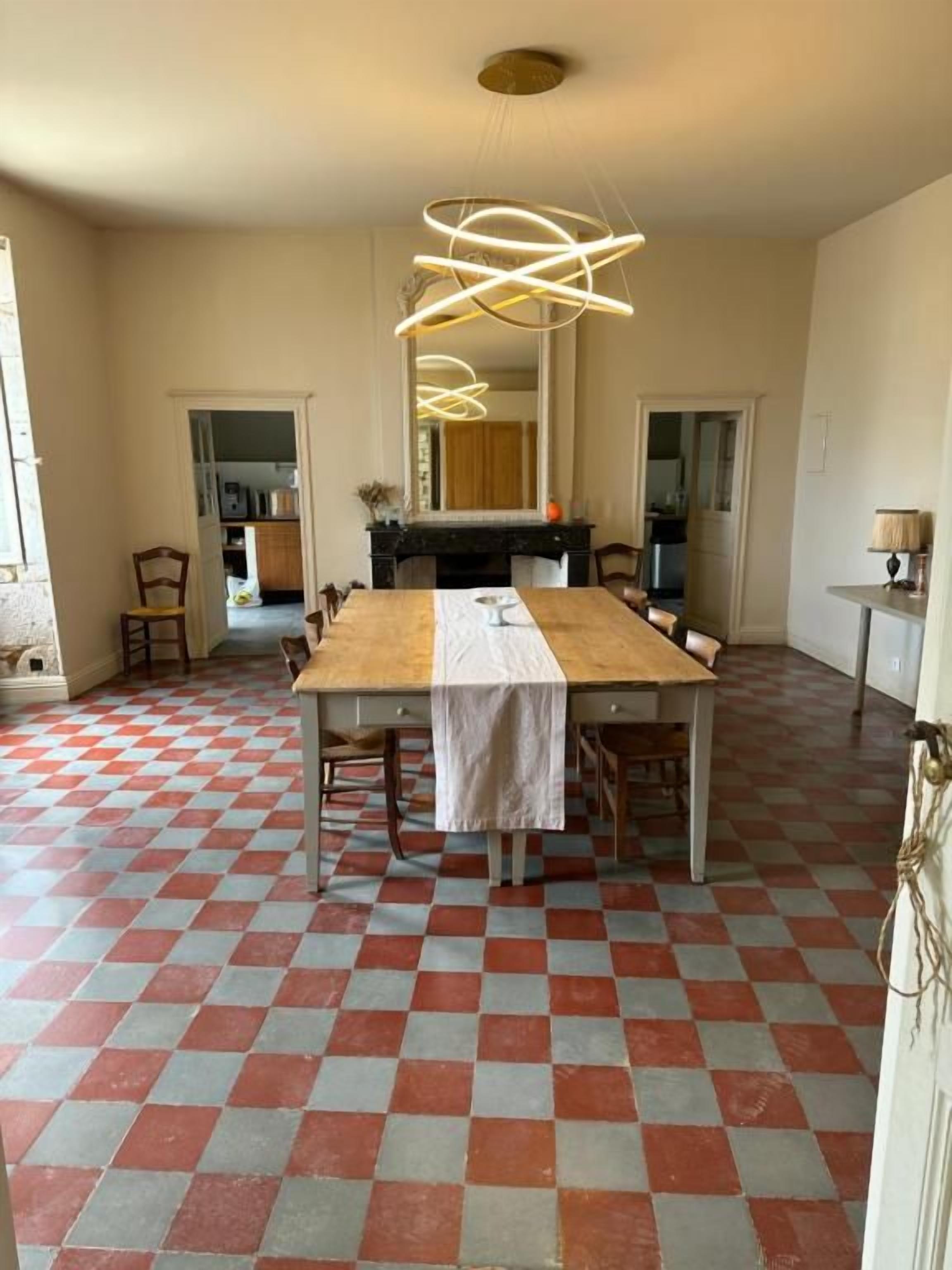 Zona pranzo con pavimento a scacchi, tavolo in legno, sedie e lampada a sospensione moderna.