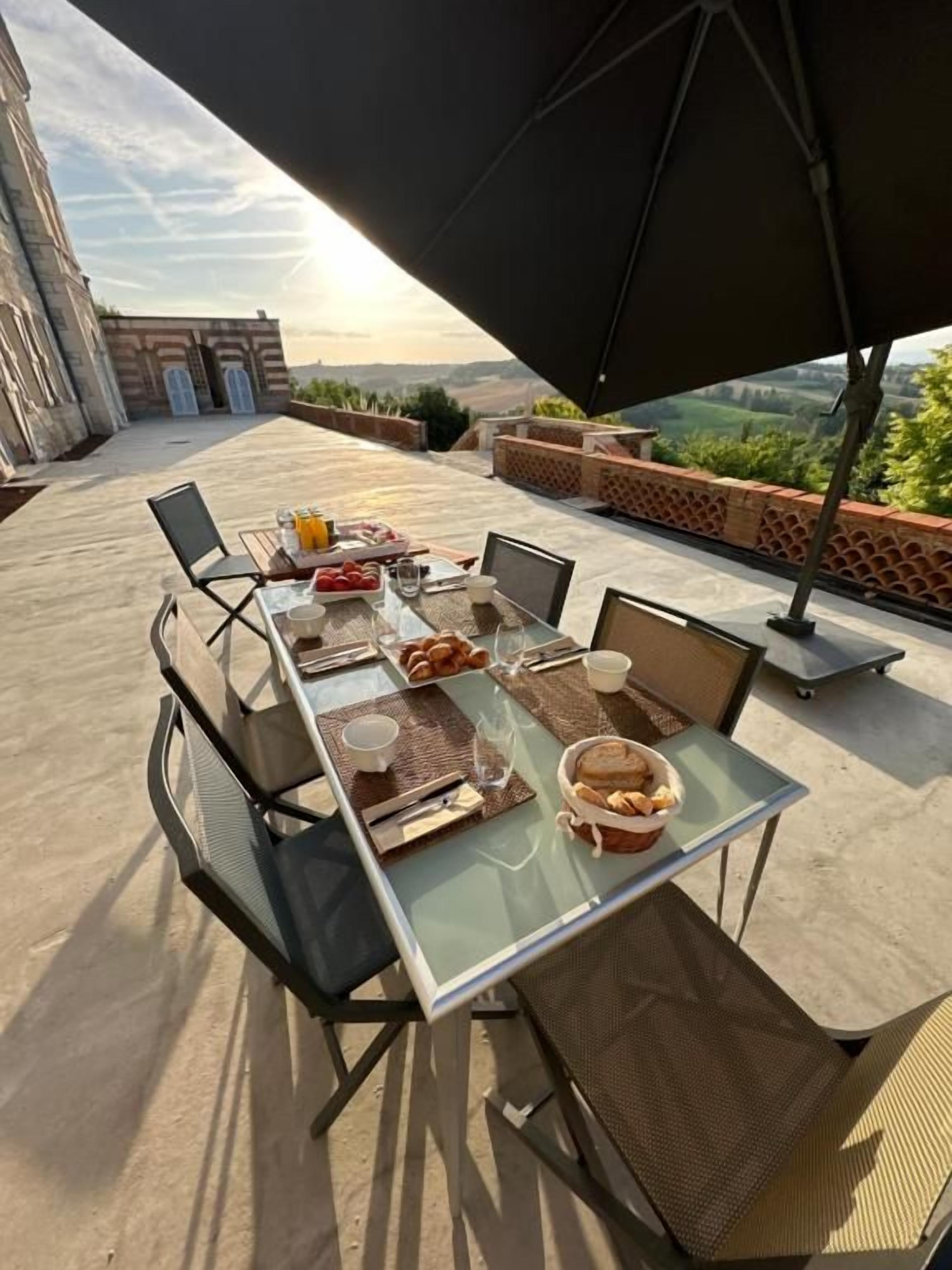 Un'area pranzo all'aperto con un tavolo apparecchiato per due, un ombrellone che offre ombra e vista sul paesaggio.