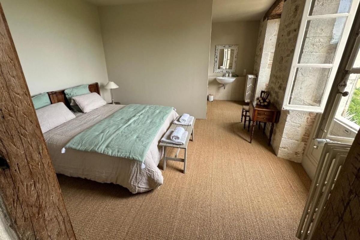 A bedroom with a bed, bedside tables, a lamp, a mirror, a window, and a door.