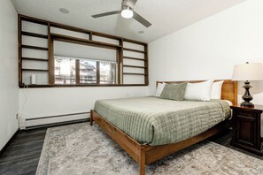 A bedroom with a bed, a nightstand, a lamp, a window with blinds, and a ceiling fan. - Golf Course Retreat | Hot Tub, Mtn Views, 5BR (Estes Park)