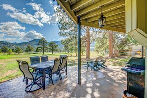 Patio esterno con tavolo e sedie, un barbecue e vista su un prato e montagne.