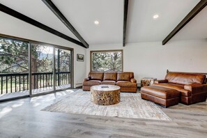 A spacious living room with a large sectional sofa, a round coffee table, and a view through large sliding glass doors to the outdoors. - Golf Course Retreat | Hot Tub, Mtn Views, 5BR (Estes Park)