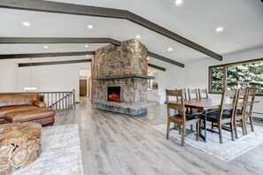 A spacious living area with a stone fireplace, wooden dining table, and leather sofa. - Golf Course Retreat | Hot Tub, Mtn Views, 5BR (Estes Park)