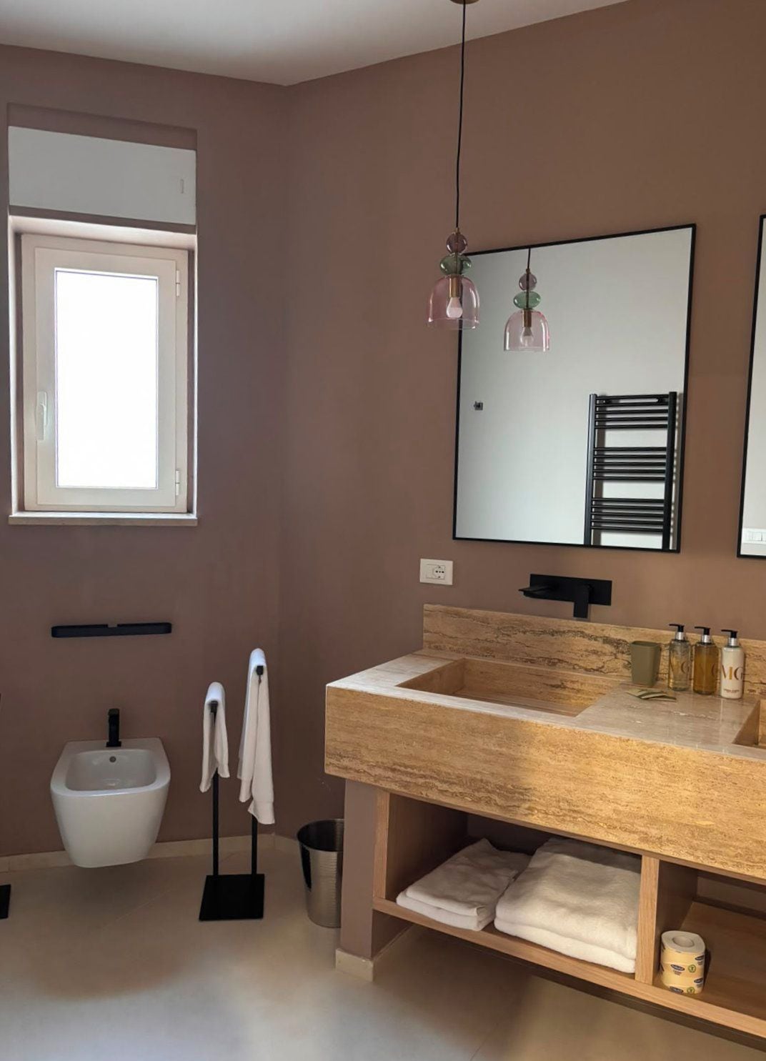 A modern bathroom with a large mirror, a sink with a wooden countertop, a bidet, and a towel rack.
