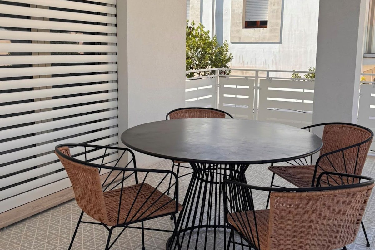 A round table with four chairs, a white wall with a window, and a geometric patterned floor.