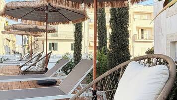 A rooftop terrace with wicker lounge chairs, thatched umbrellas, and a view of buildings.
