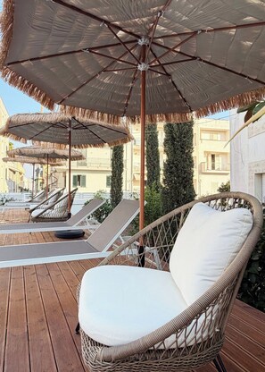 Una terraza en la azotea con sillones de mimbre, sombrillas de paja y vistas a edificios.