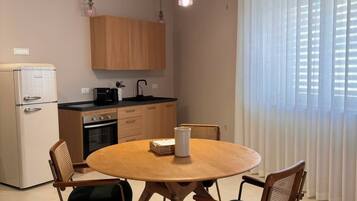 Une cuisine compacte avec un coin repas, comprenant une table ronde en bois entourée de quatre chaises, un réfrigérateur, une cuisinière et un luminaire suspendu.