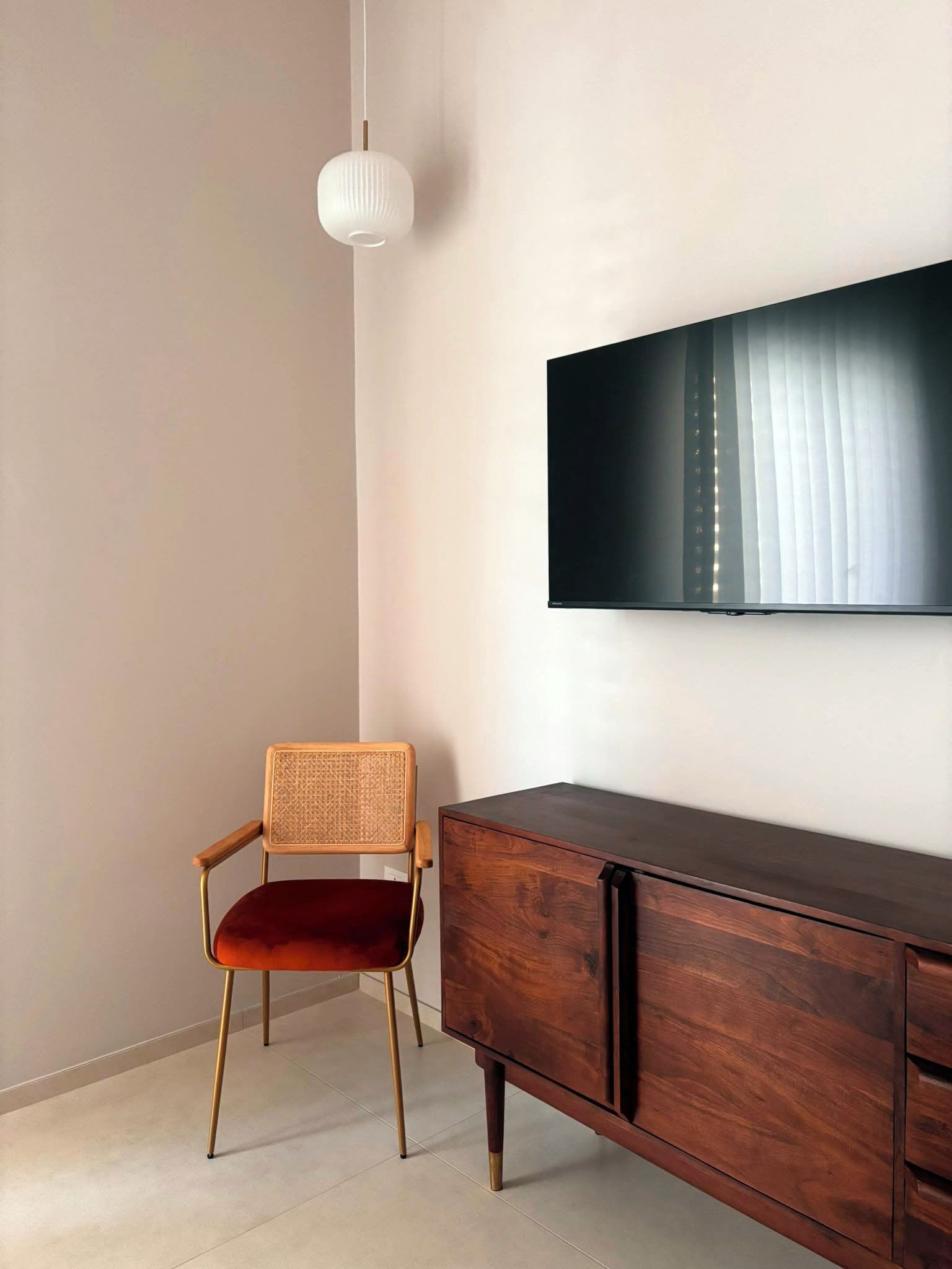 Una habitación con un armario de madera, un televisor montado en la pared y una silla de mimbre.