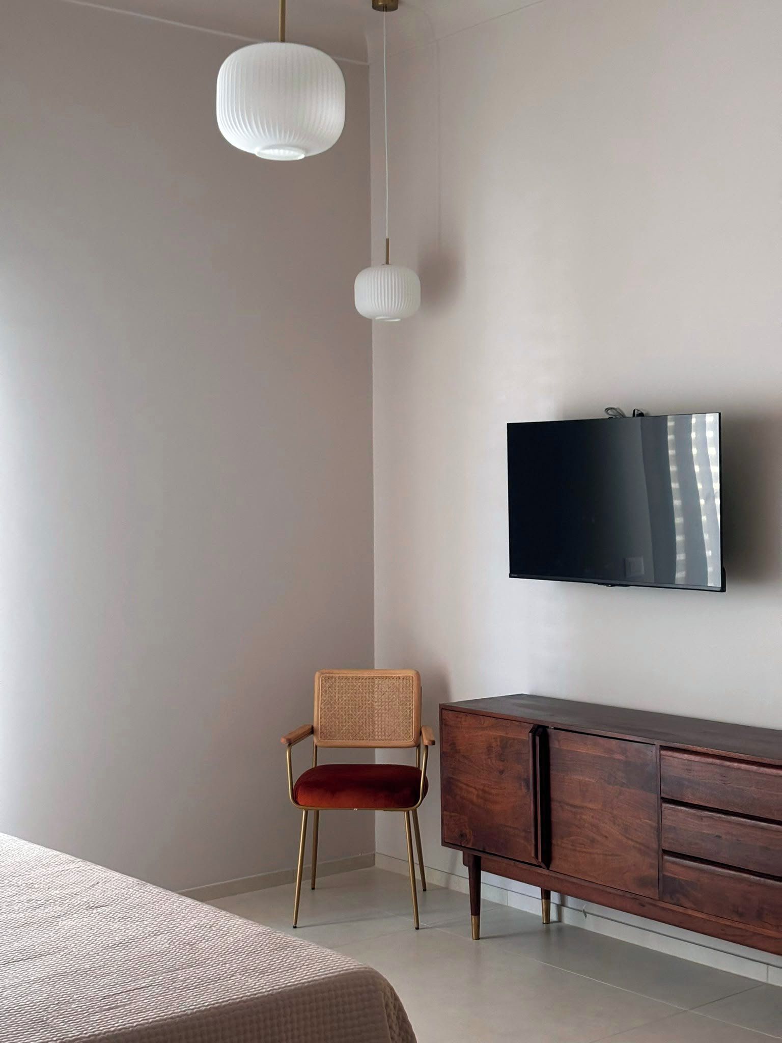 A bedroom with a bed, a television mounted on the wall, a wooden dresser, and a chair.