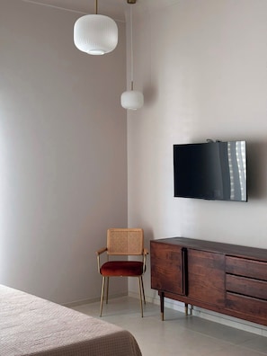 Un dormitorio con cama, televisor montado en la pared, cómoda de madera y una silla.