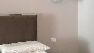 Una cama bien hecha con ropa de cama blanca, un cabecero marrón, una mesita de noche y una lámpara colgante blanca.