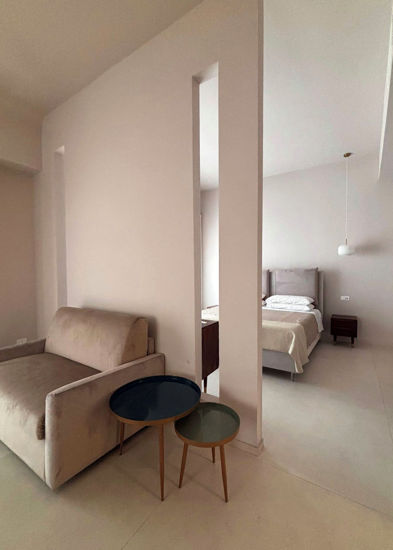 Una sala de estar moderna con un sofá, una mesita redonda y una cama al fondo.