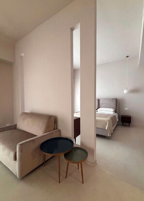 Una sala de estar moderna con un sofá, una mesita redonda y una cama al fondo.