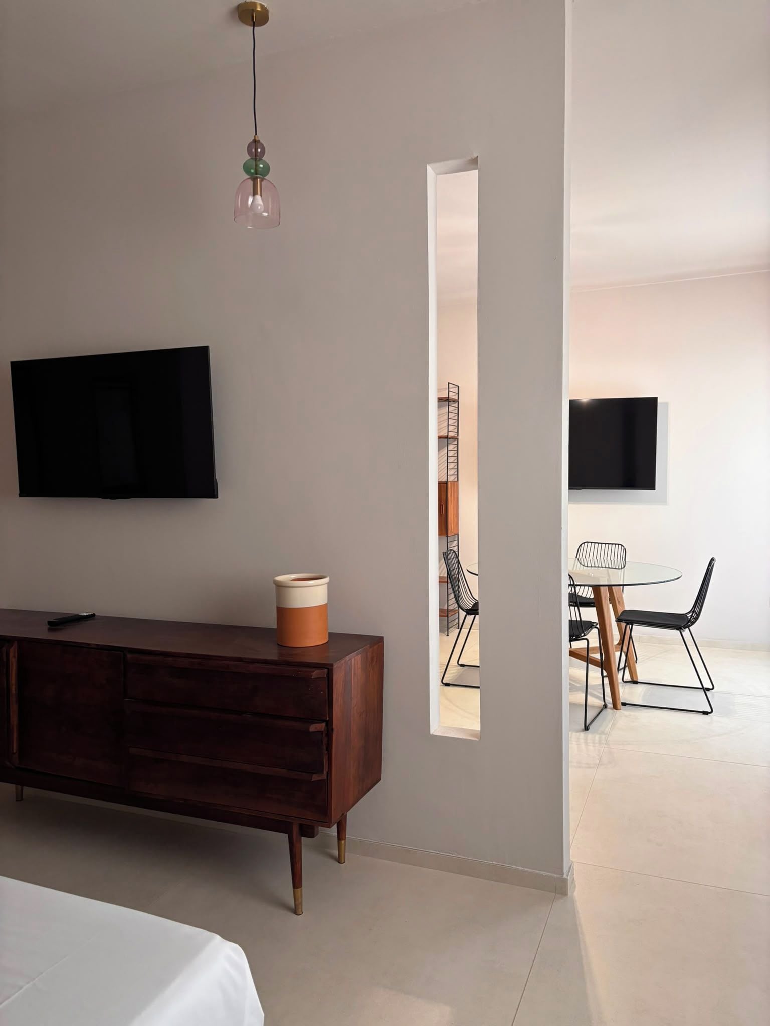 Habitación de hotel moderna con una cama grande, un televisor de pantalla plana montado en la pared, un aparador de madera y una pequeña mesa con sillas.