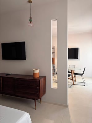 Habitación de hotel moderna con una cama grande, un televisor de pantalla plana montado en la pared, un aparador de madera y una pequeña mesa con sillas.