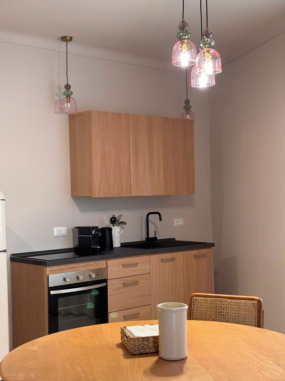 Una cocina moderna con armarios de madera, encimera negra y una mesa de comedor con una jarra blanca.