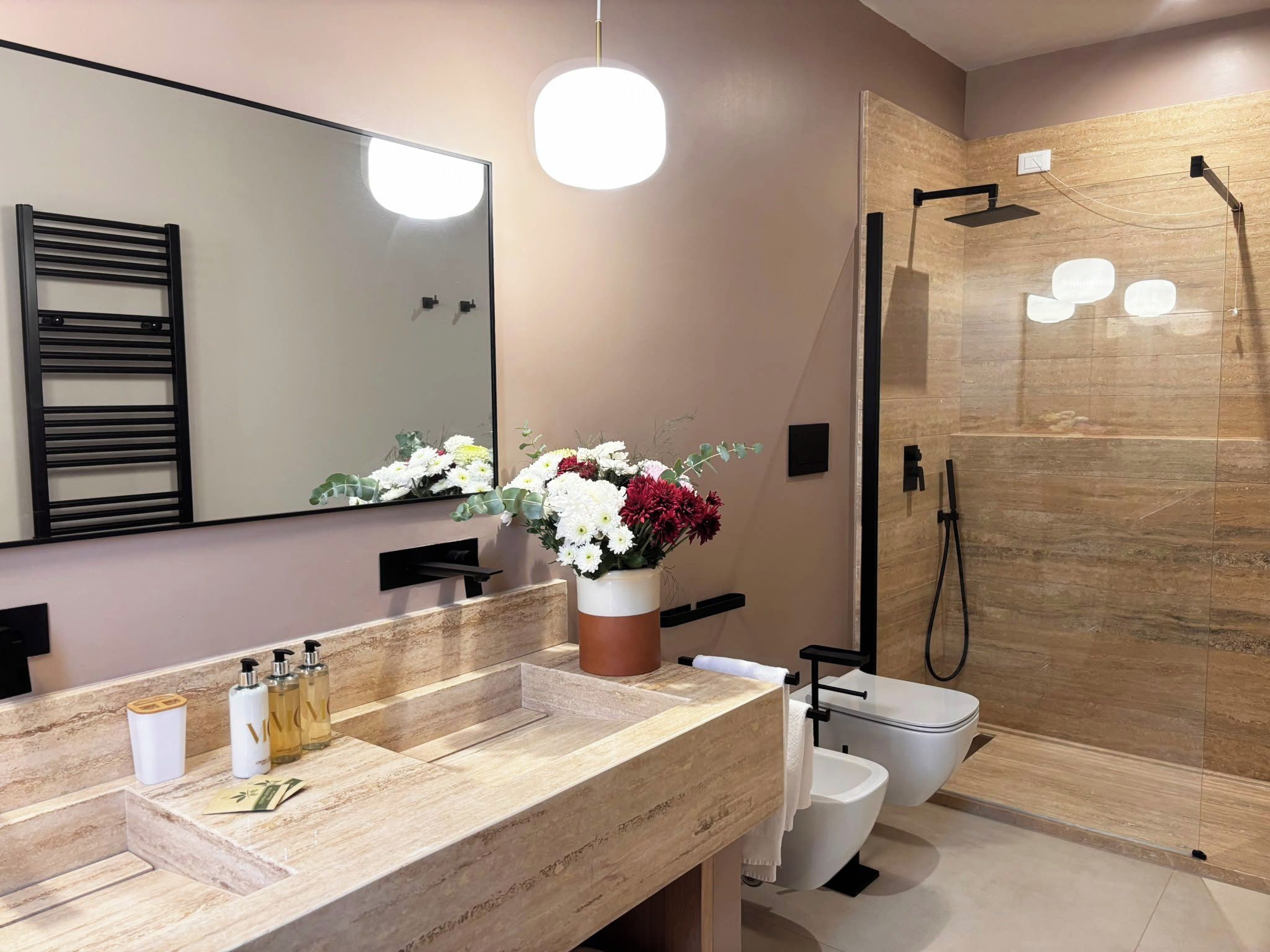 A modern bathroom with a large mirror, a shower with a glass door, and a vanity with a beige countertop.