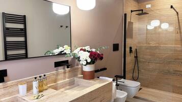 A modern bathroom with a large mirror, a shower with a glass door, and a vanity with a beige countertop.