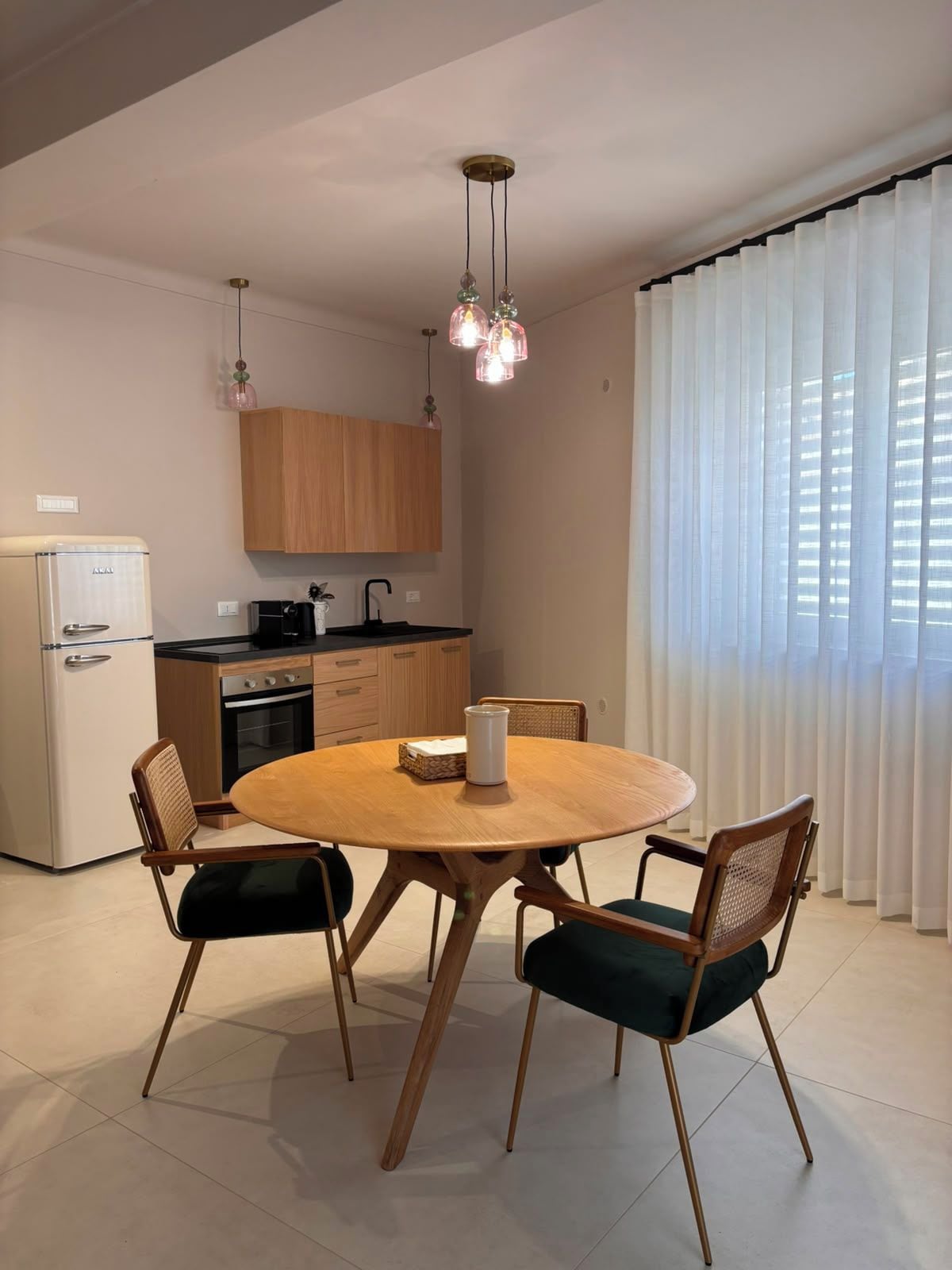 Een compacte keuken met een eethoek, met een ronde houten tafel met vier stoelen, een koelkast, een kookplaat en een hangende hanglamp.