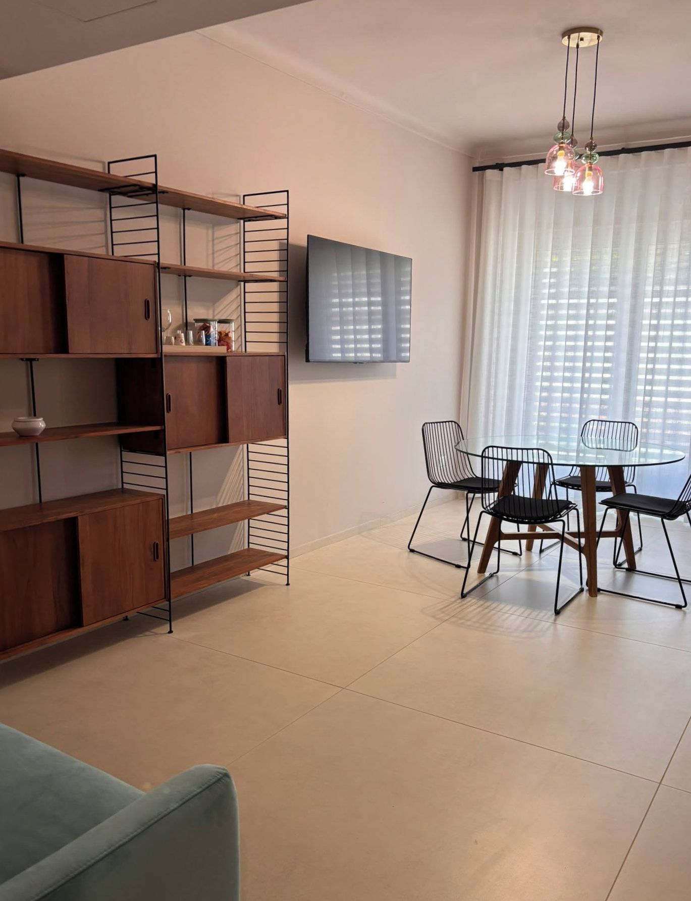Una sala de estar moderna con comedor, que incluye un televisor montado en la pared, una mesa de comedor con sillas y estanterías empotradas de madera.
