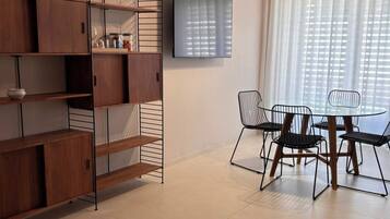 Una sala de estar moderna con comedor, que incluye un televisor montado en la pared, una mesa de comedor con sillas y estanterías empotradas de madera.