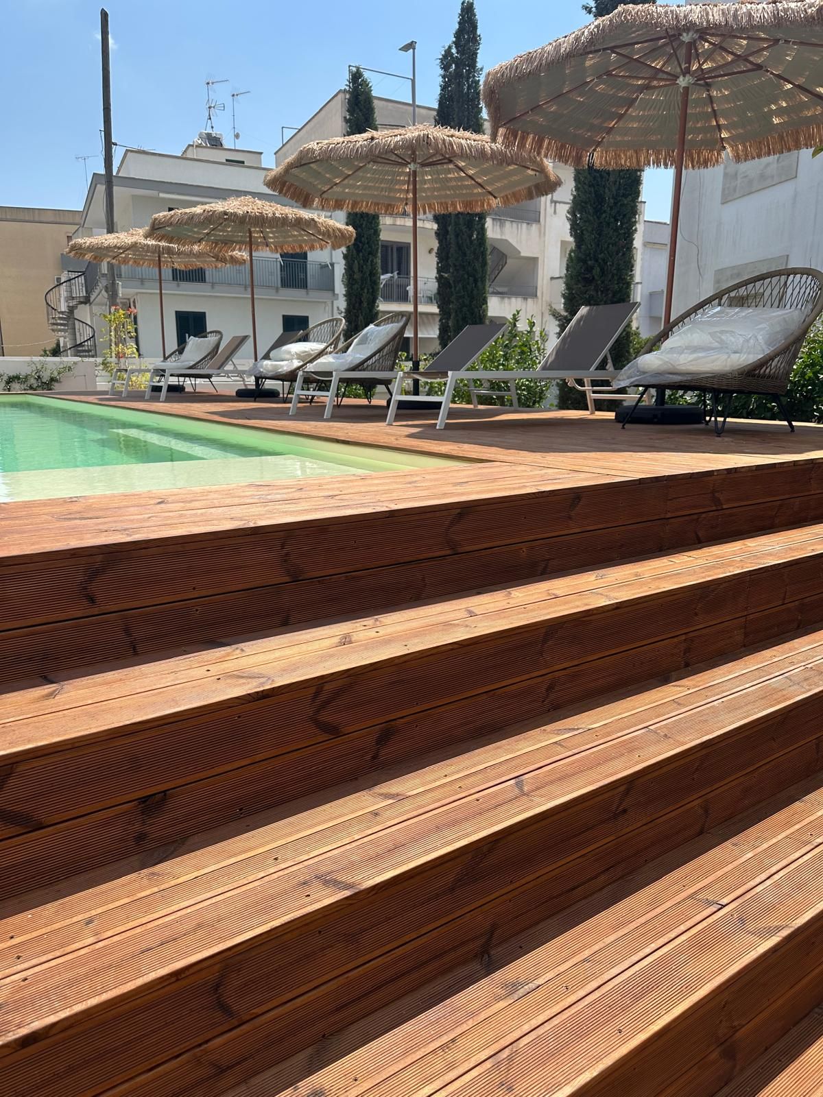 A poolside area with wooden steps leading to lounge chairs and umbrellas.