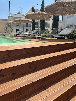 Zona de piscina con escalones de madera que llevan a sillas de descanso y sombrillas.