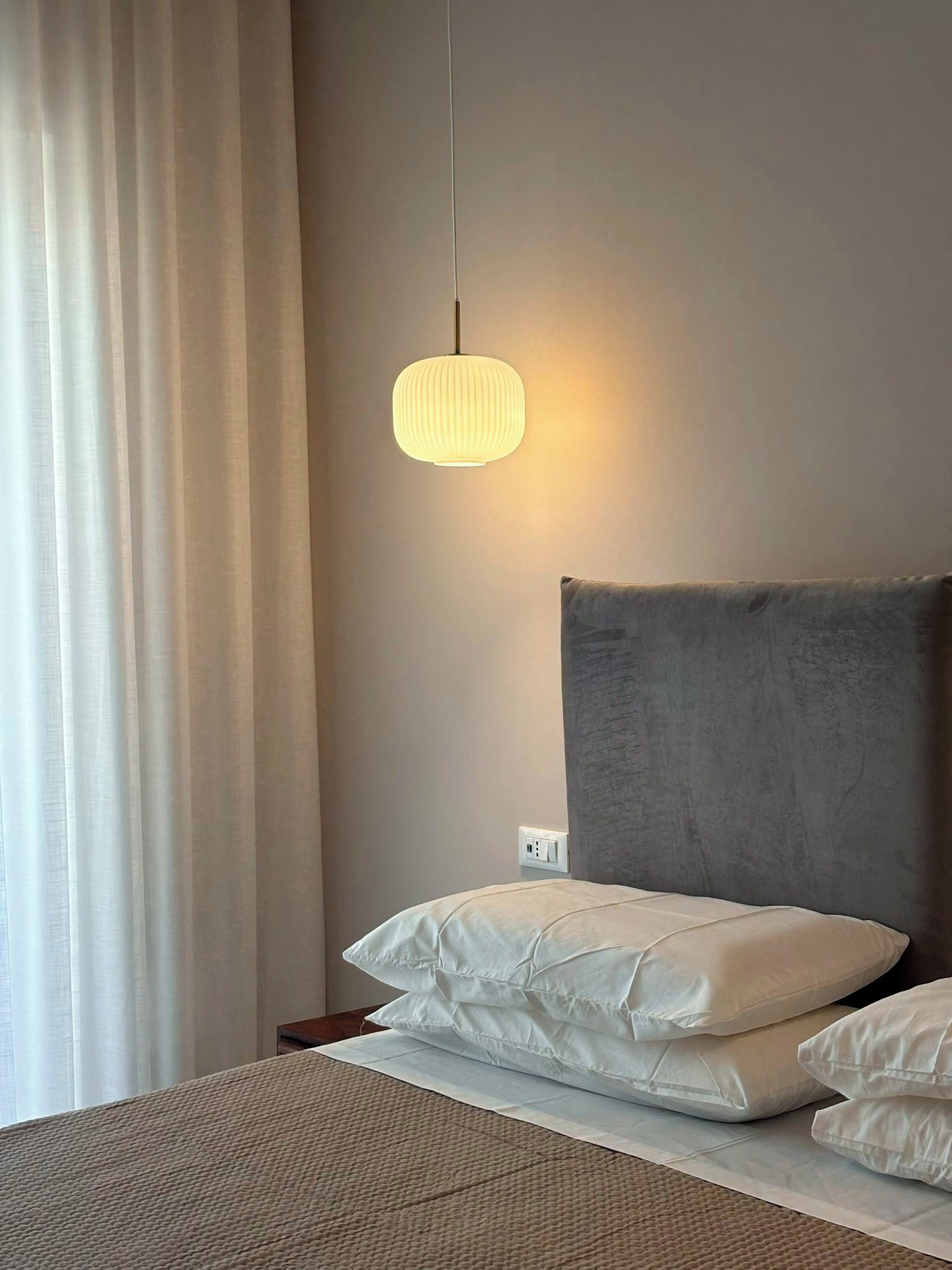 A bedroom with a bed, a bedside table, a lamp, and a window with curtains.