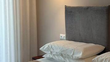 A bedroom with a bed, a bedside table, a lamp, and a window with curtains.