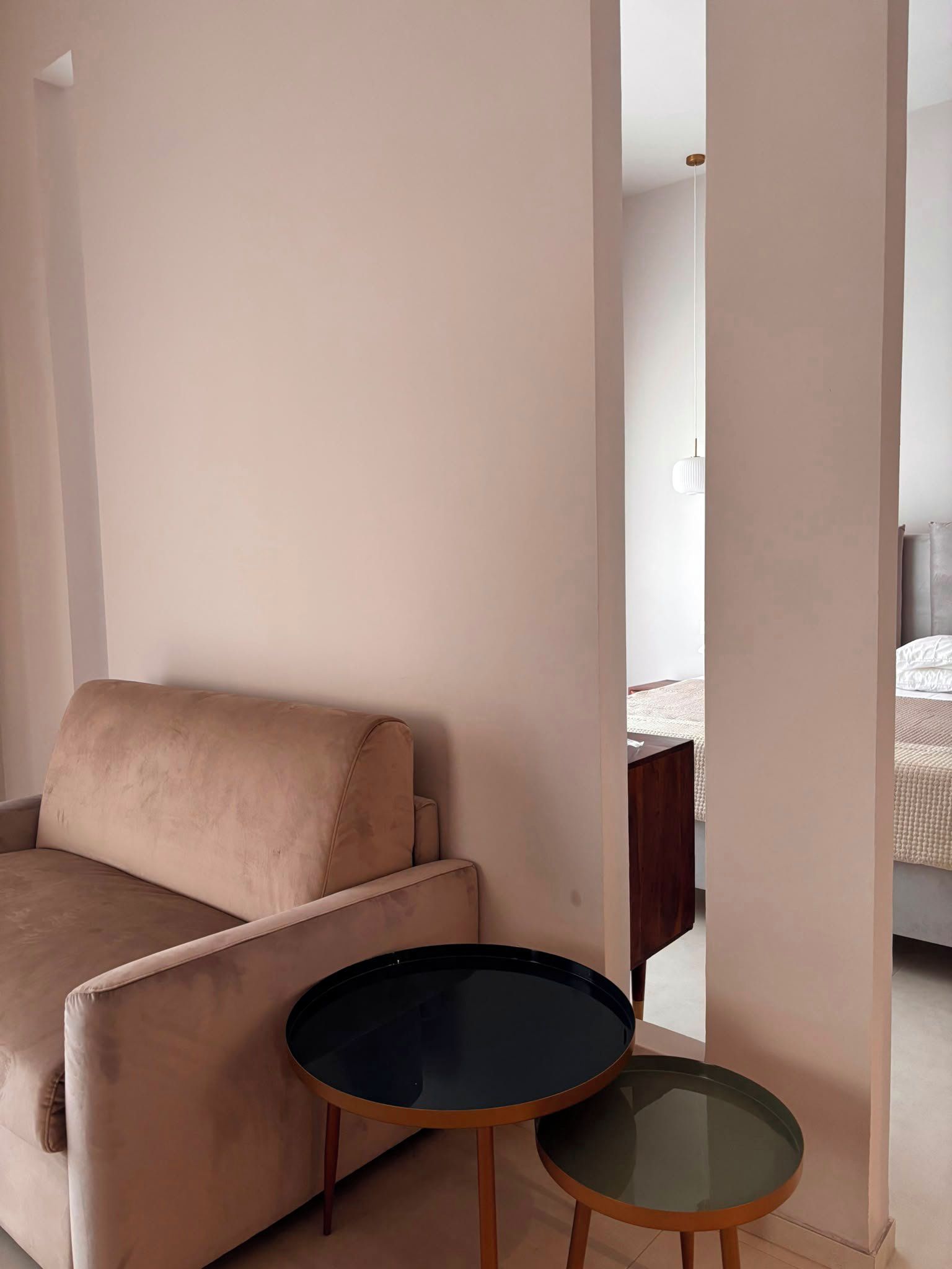 A room with a beige sofa, a small round table, and a bed with a white duvet.