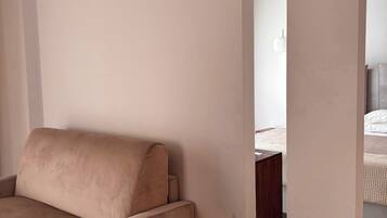 A room with a beige sofa, a small round table, and a bed with a white duvet.