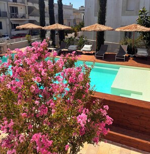 Zona de piscina al terrat amb gandules i ombrelles, envoltada de plantes florides de color rosa.