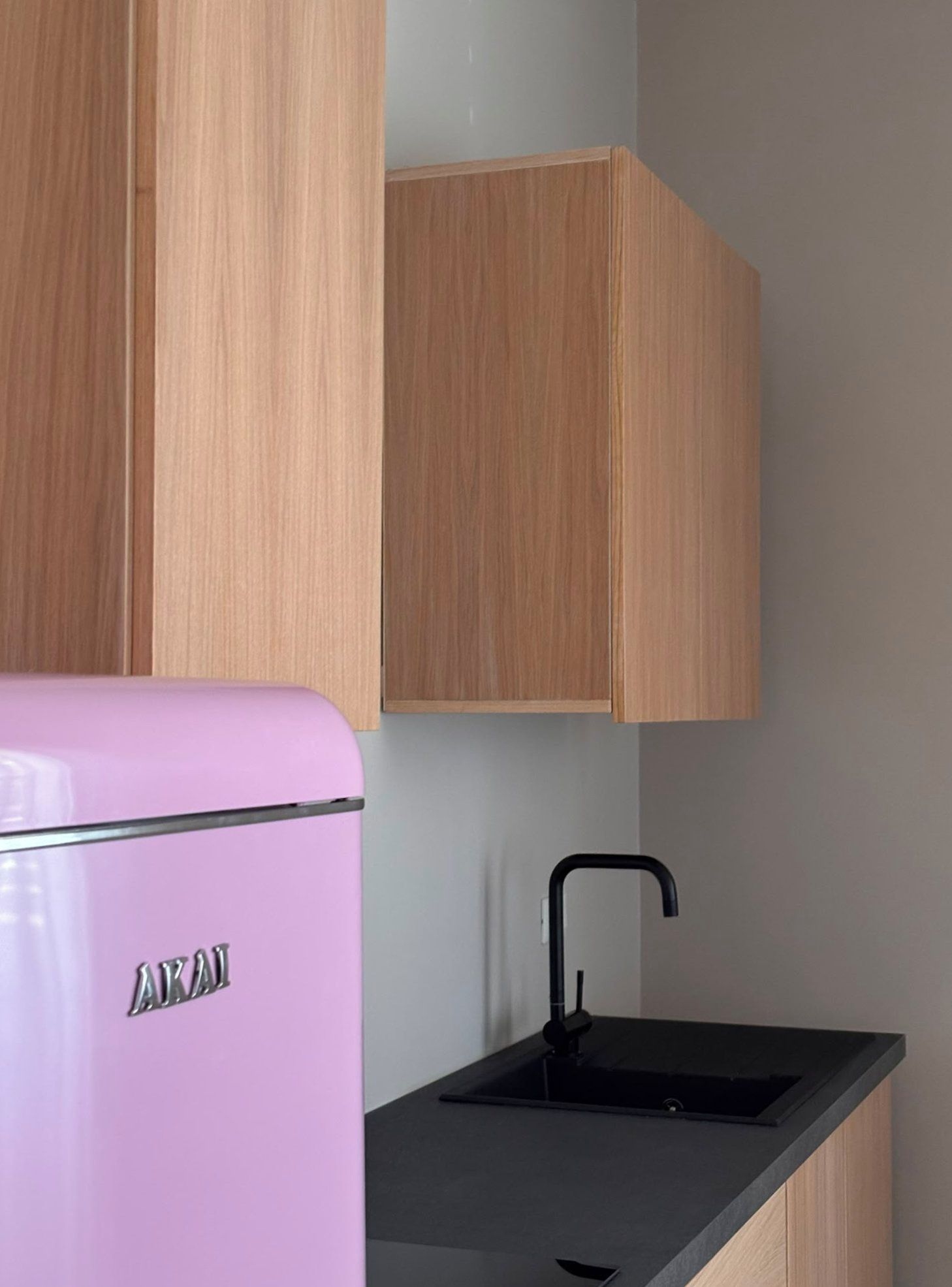 Una cocina con armarios de madera, un refrigerador rosa y un lavamanos negro.