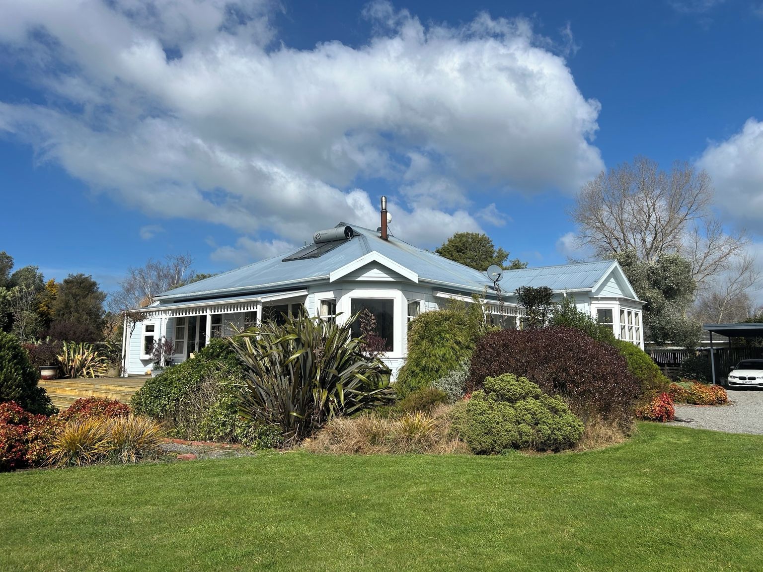 A white house with a blue roof, surrounded by a well-maintained garden and trees.