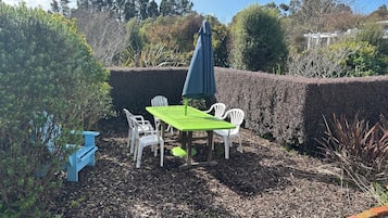 An outdoor seating area with a table and chairs, surrounded by a hedge and trees.