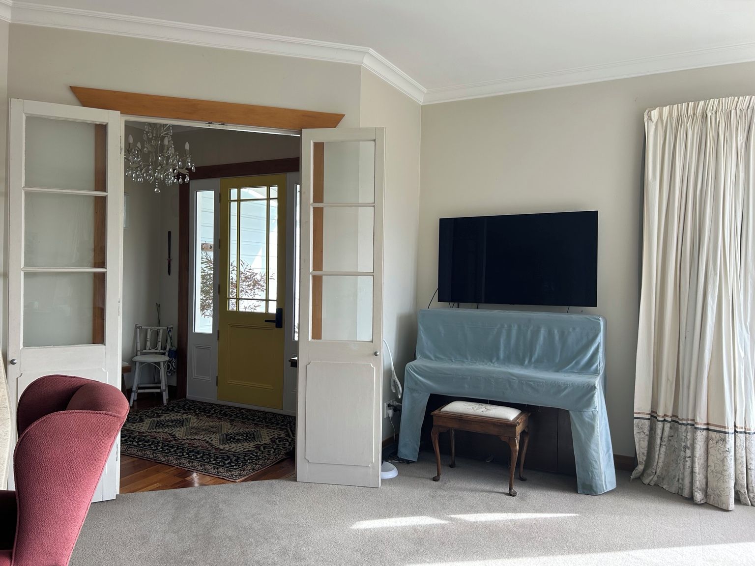 A room with a television mounted on the wall, a door leading to another room, a chair, and a small table.