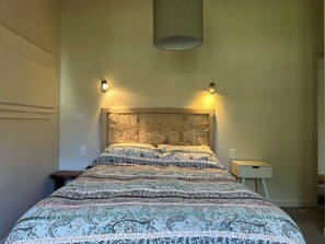 Una cama con una colcha estampada, dos lámparas de pared y una mesita de noche con lámpara.