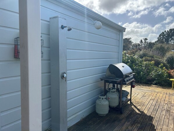 A metal door with a handle and a peephole, a barbecue grill, and two propane tanks on a wooden deck.